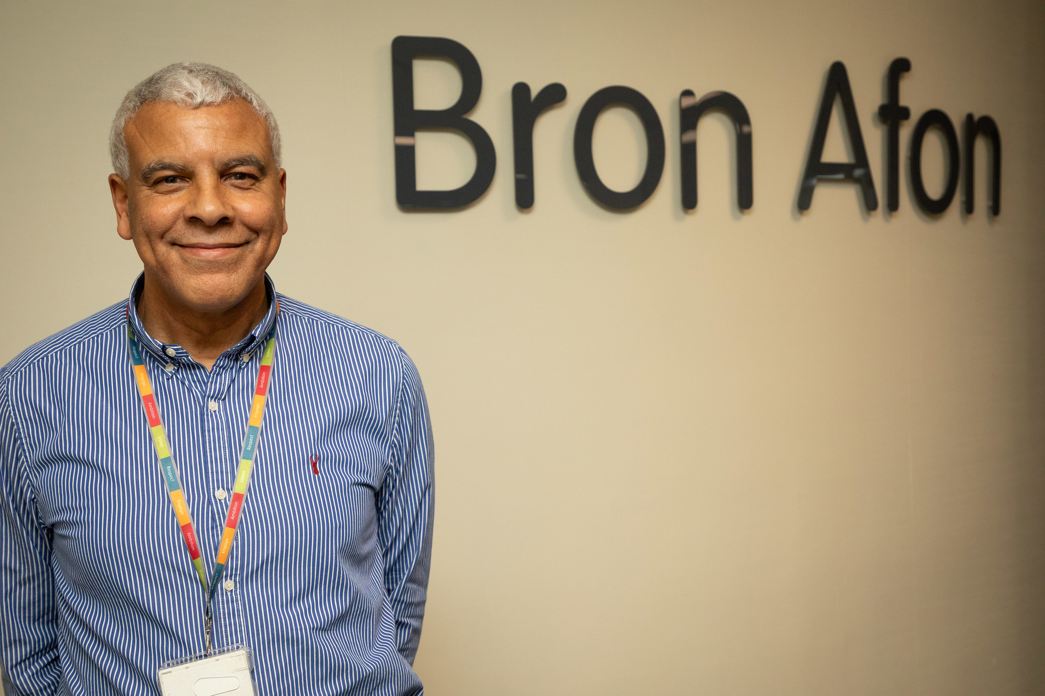 Smiling man in a striped shirt standing in front of a Bron Afon wall sign